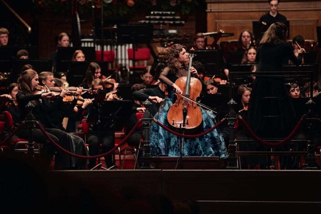 lady playing a cello with an orchestra
